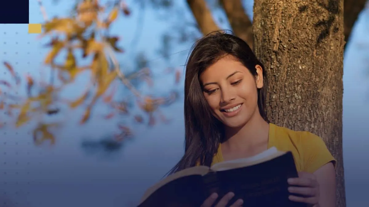Estudiante leyendo un libro bajo un árbol para inspirarse en la dedicatoria de su tesis