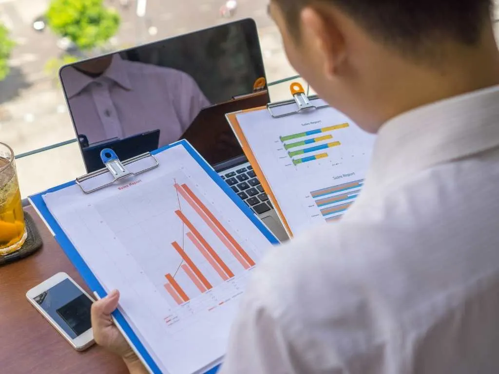 Persona analizando gráficos y tablas de datos estadísticos impresos, con laptop y móvil, para interpretar la relación entre variables en una investigación correlacional.