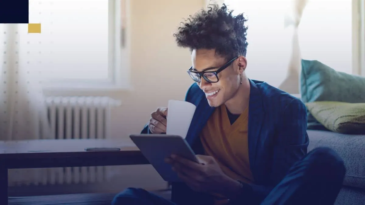 Estudiante universitario sentado en casa, tomando café y revisando ideas de temas para tesis en una tablet.