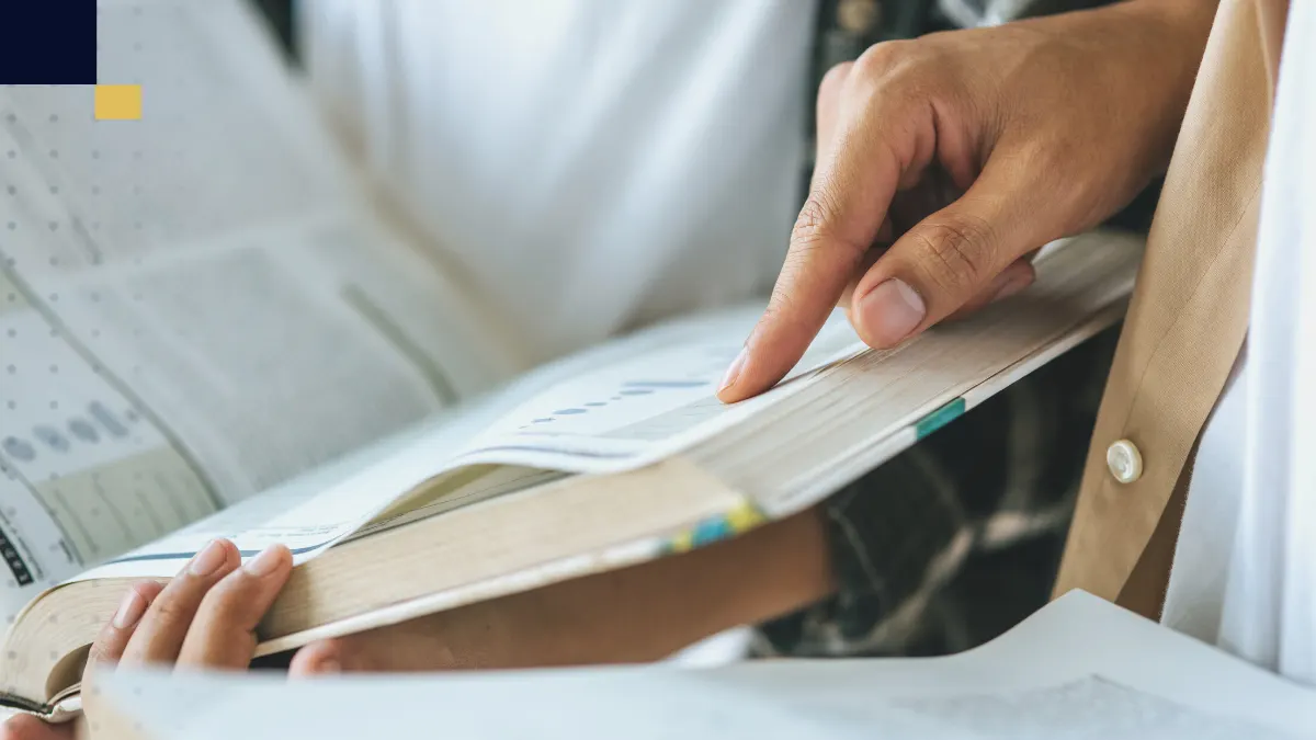 Estudiante universitaria reflexionando y tomando notas en una libreta, revisando recursos digitales para definir y delimitar el tema de su tesis.