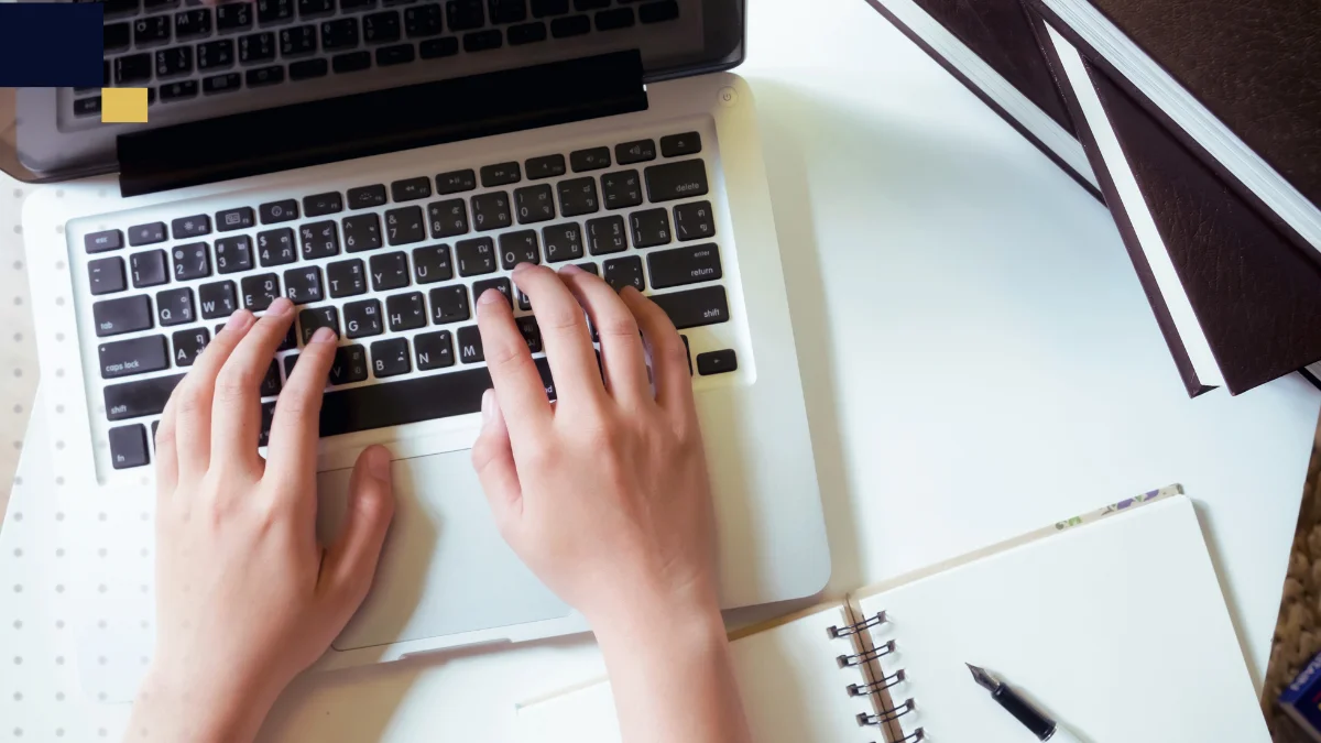 Persona escribiendo en una laptop junto a un cuaderno y material de estudio, imagen de Tesis y Másters Colombia sobre asesoría, corrección y apoyo académico para tesis y proyectos universitarios.
